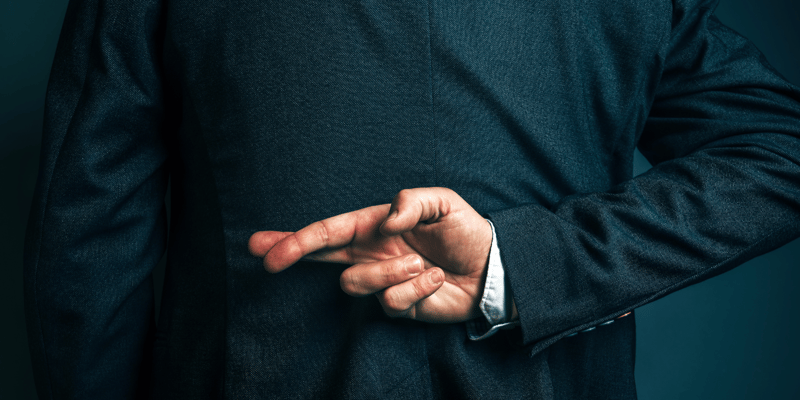 Picture of a businessman crossing his fingers behind his back, in a visualisation of dishonesty.